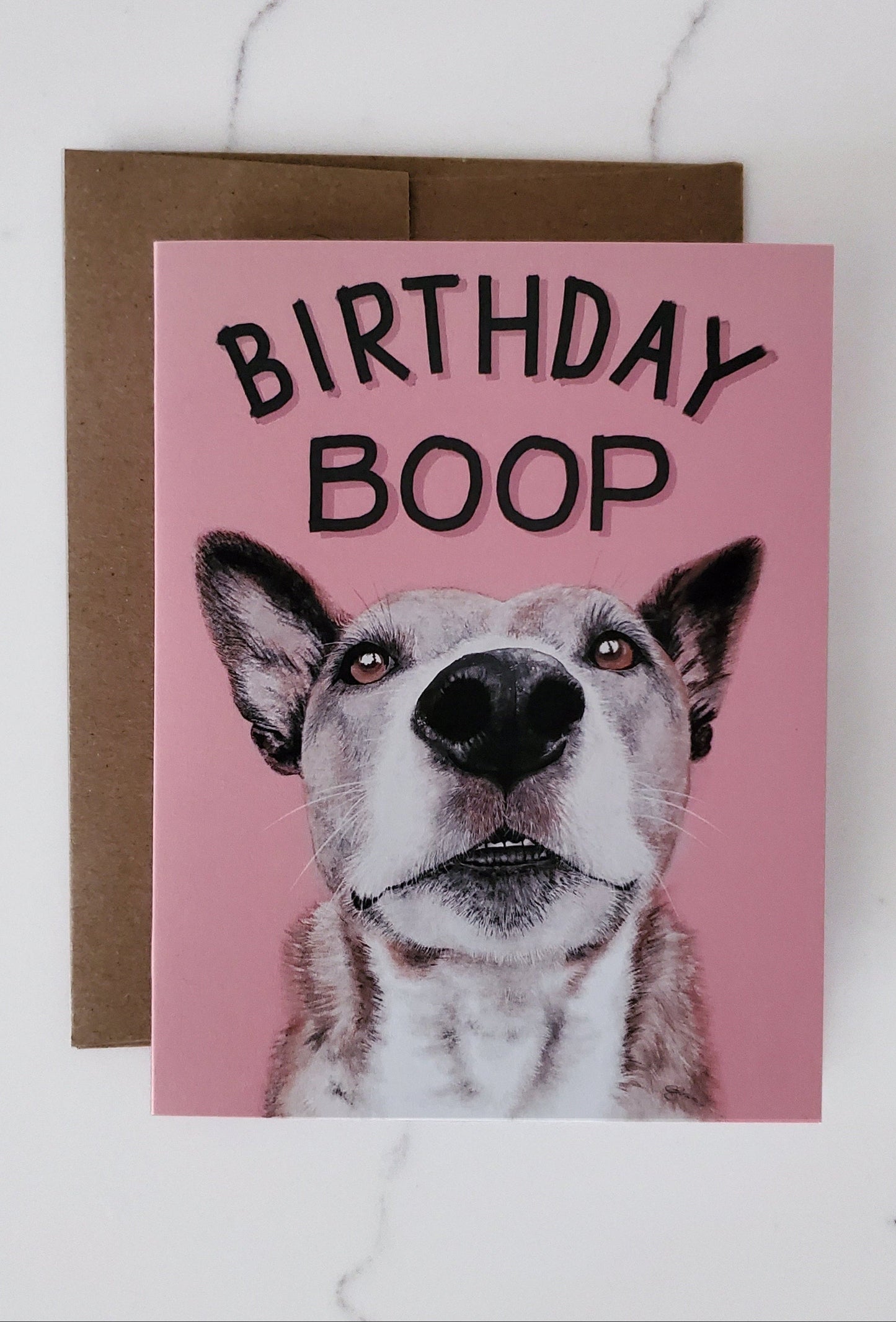 A greeting card with a close-up image of a dog's nose and the text 'BIRTHDAY BOOP' on it, accompanied by a brown kraft paper envelope.
