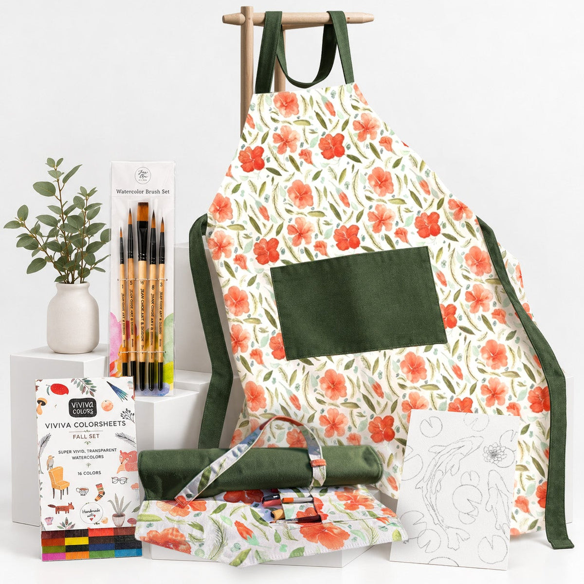 A watercolor painting kit set up on a white background, featuring a large apron with a floral print, a watercolor brush set, a set of Viviva Colorsheets, a rolled-up green canvas artist's tool case, and a coloring page on a wooden stand.