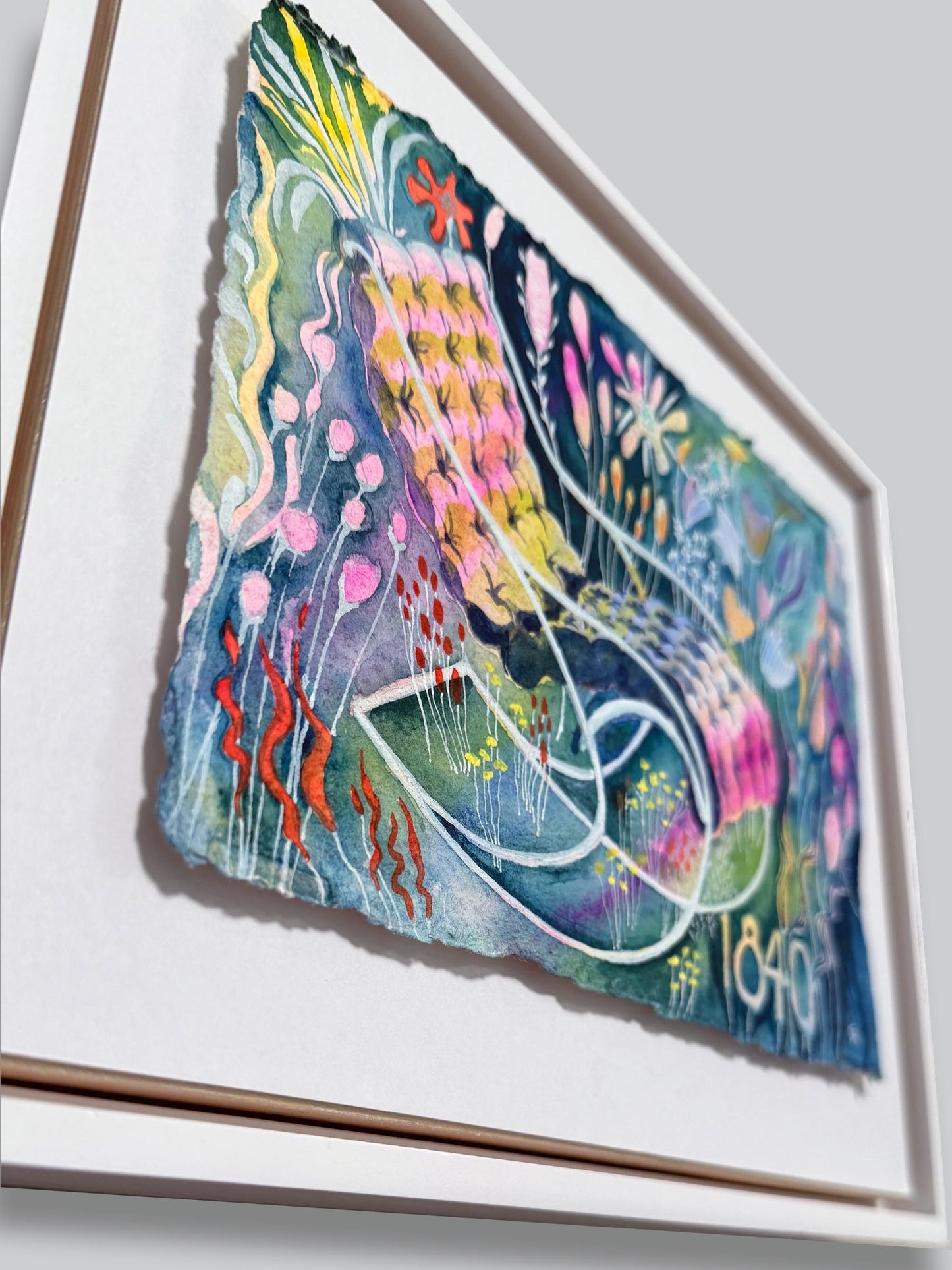 Framed artwork with colorful abstract design on a white wall. lots of color watercolor on a recycled cotton cold press textured paper with raw ripped edge. florals surround a lounge tufted chair with curvy classic lines from 1840
