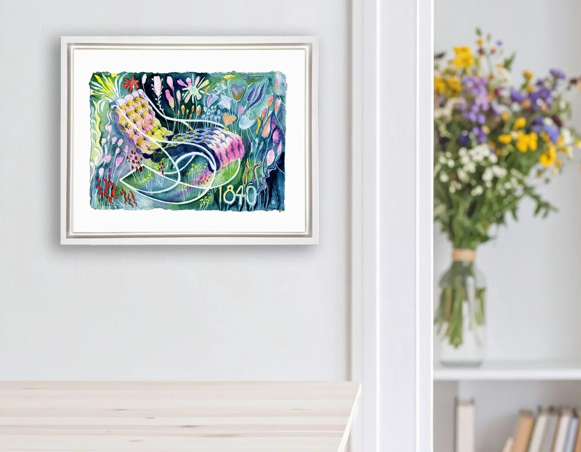 Framed colorful abstract artwork on a wall next to a white shelf with books and a vase of flowers.