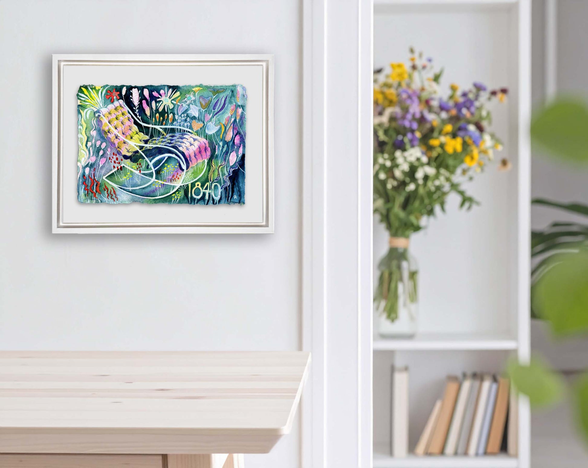 Framed artwork with colorful floral around a chair design on a white wall. bouquet in the background next to a large house plant. bookshelf and books, kitchen table in light wood. lots of color watercolor on a recycled cotton cold press textured paper with raw ripped edge. florals surround a lounge tufted chair with curvy classic lines from 1840