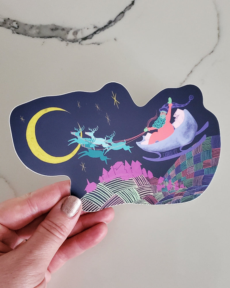vinyl die cut santa christmas holiday sticker village below reindeer pulling sleigh flying through sky on the way to a sliver yellow moon hills below are multicolored and textured like a fluffy patchwork quilt santa waving
